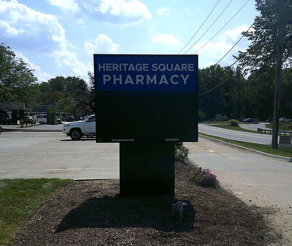 A sign for Heritage Square Pharmacy that combines a monument sign base with a LED lit header on top of an electric message center