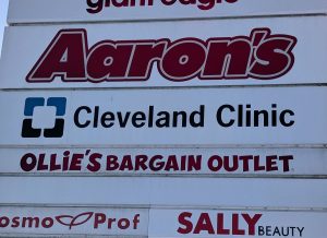 Close-up of the Cleveland Clinic tenant panel installed on the Heritage Square plaza monument sign in Dover, Ohio, showing the Cleveland Clinic logo and wordmark alongside neighboring tenant panels