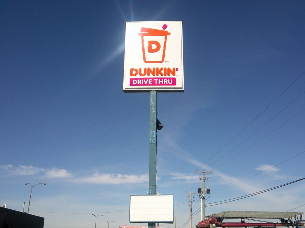 Tall single-pole cabinet sign displaying Dunkin' branding and Drive Thru panel against a clear blue sky in New Philadelphia, Ohio by Adams Signs & Graphics