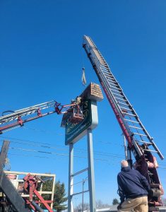 Adams Signs crew removes the old cabinet sign face from a pole-mounted sign structure using a crane and aerial lift in Massillon, Ohio