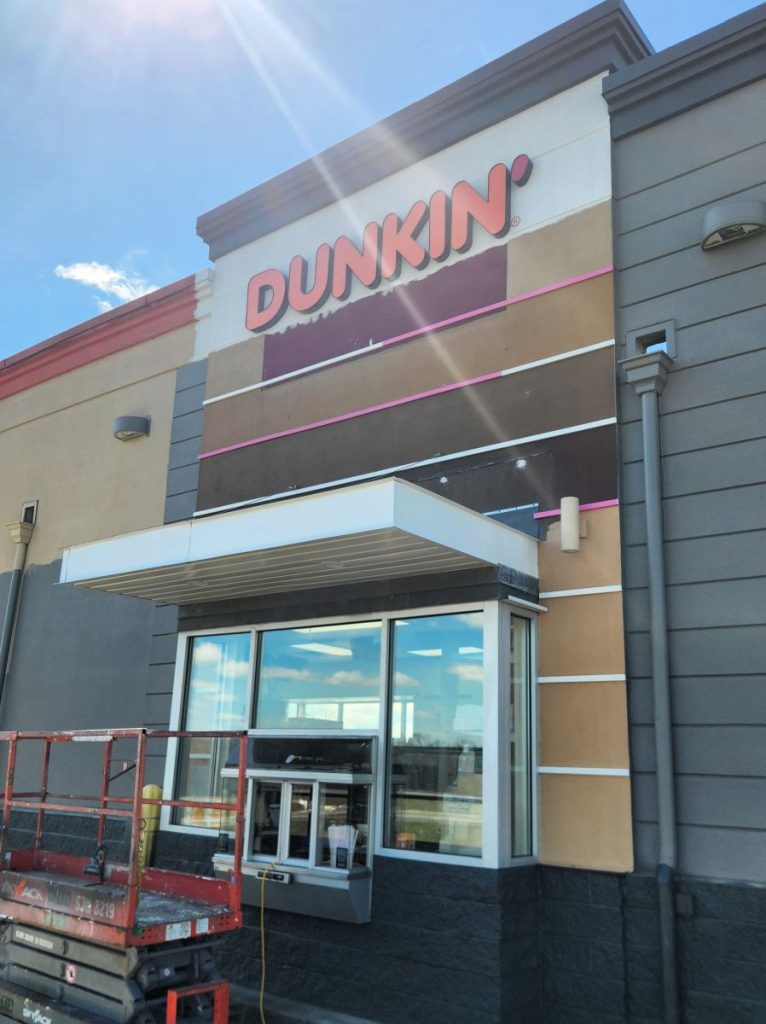 Dunkin' building cabinet sign freshly installed above the store entrance in Poland, Ohio, photographed during installation with a scissor lift visible | Adams Signs & Graphics