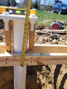 Sign post anchor bolts being measured and leveled with a tape measure and spirit level during ground installation, with bracing lumber and power tools visible at the job site | Adams Signs & Graphics