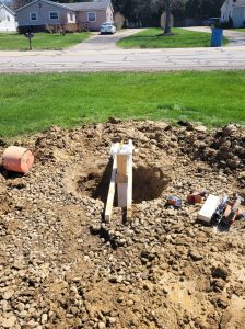 Wide view of an excavated hole with a braced sign post and base plate centered and ready for concrete, with installation tools and gravel surrounding the job site in Akron, Ohio | Adams Signs & Graphics