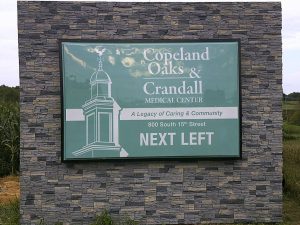 A finished stone veneer monument sign for Copeland Oaks and Crandall Medical Center displaying a directional message reading next left | Adams Signs & Graphics