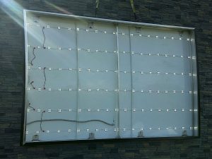 An illuminated sign cabinet being installed on a stone facade showing rows of LED modules and wiring inside the panel | Adams Signs & Graphics