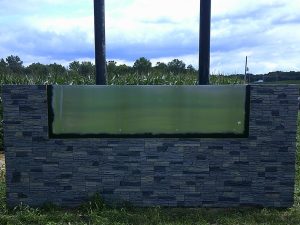 A stone veneer monument sign base under construction with a protective film covering the blank face panel in a rural setting | Adams Signs & Graphics