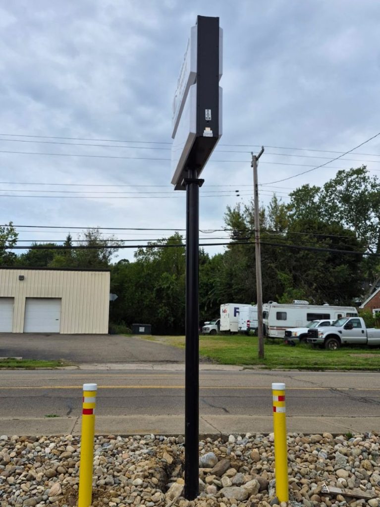 Side angle view of the Canton South Eyecare pole sign cabinet mounted on its black pole with protective bollards in the foreground | Adams Signs & Graphics