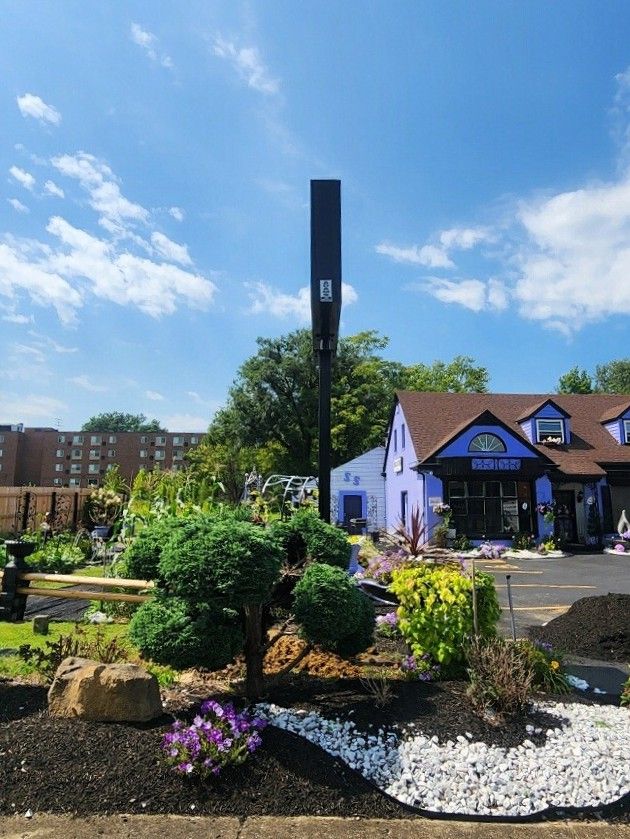 Side angle view of the pole sign for Show Stopper Garden Center rising above landscaped shrubs and stone accents | Adams Signs & Graphics
