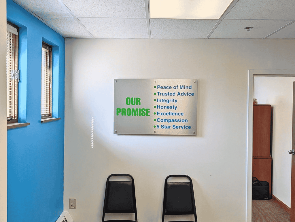 Brushed aluminum Our Promise sign with green and blue lettering mounted on standoffs above two waiting room chairs in the HealthMarkets office | Adams Signs