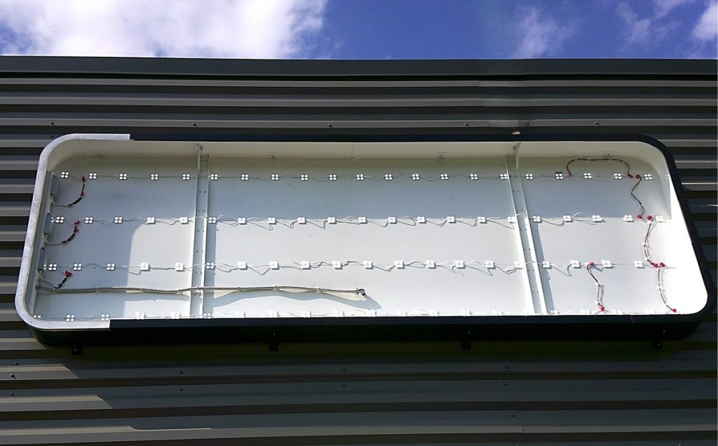 Open sign cabinet mounted on a dark metal building showing rows of white LED modules and wiring during installation | Adams Signs & Graphics