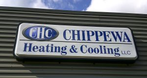 Illuminated cabinet sign with a blue CHC oval logo and Chippewa Heating & Cooling LLC lettering mounted above a door on a metal building | Adams Signs & Graphics