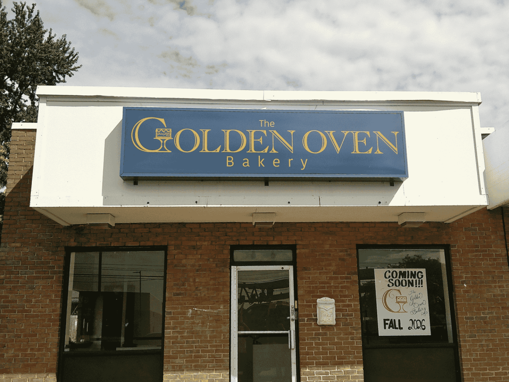 Brick bakery storefront with a blue and gold wall sign for The Golden Oven Bakery above the entrance and a coming soon poster in the window | Adams Signs & Graphics