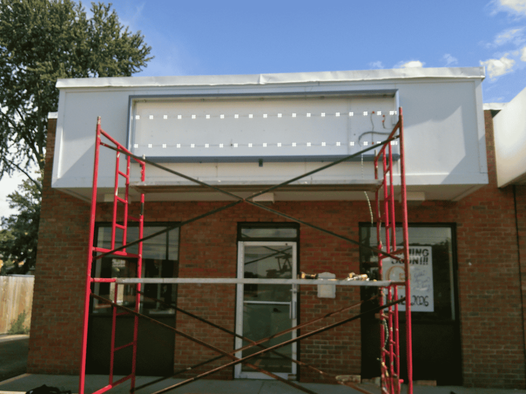 Sign cabinet fitted with rows of LED modules behind scaffolding during installation at The Golden Oven Bakery storefront | Adams Signs & Graphics